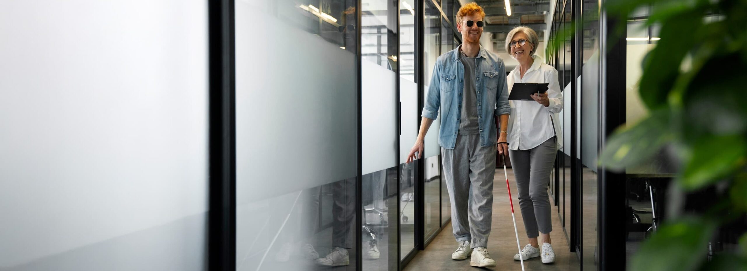 A young man uses a white cane to walk down the hall of an office building