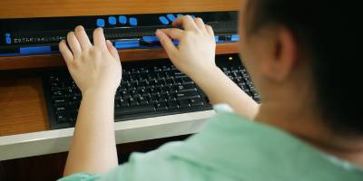 A person using a refreshable braille display alongside a computer keyboard at their workstation