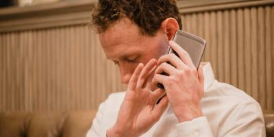 A person with a visual disability holding a smartphone close to their ear and using touch gestures.