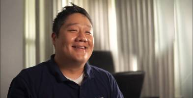 A person with a visual disability smiling while seated in a well-lit office